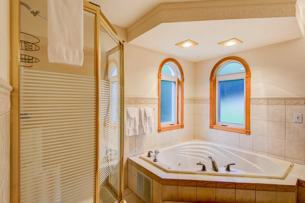 A spa-like bathroom with an inviting jacuzzi tub, framed by arched windows that fill the space with natural light. The room also features a glass shower, setting the scene for relaxation and self-care.