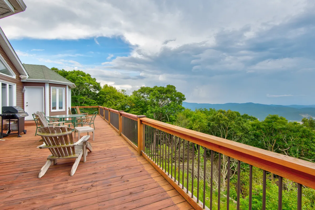 A deck with wooden flooring and metal railing offers an inviting outdoor seating arrangement, looking out to stunning mountain views. The space is perfect for relaxing with drinks, enjoying sunsets, hosting barbecues, and reading outdoors in the fresh mountain air.