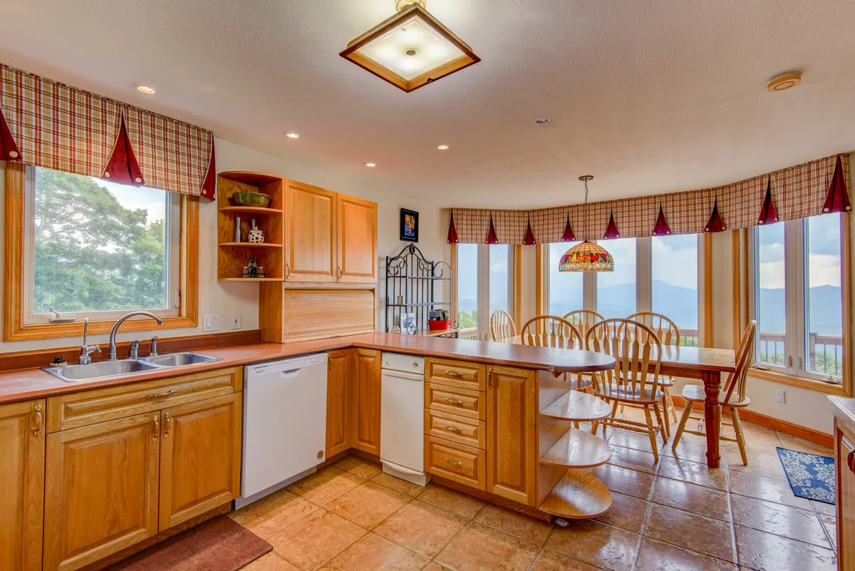 A warm, communal dining area with a large table set near big windows and a stained glass light fixture. The open layout connects seamlessly to the kitchen, bathed in natural light—perfect for shared meals and celebrations.