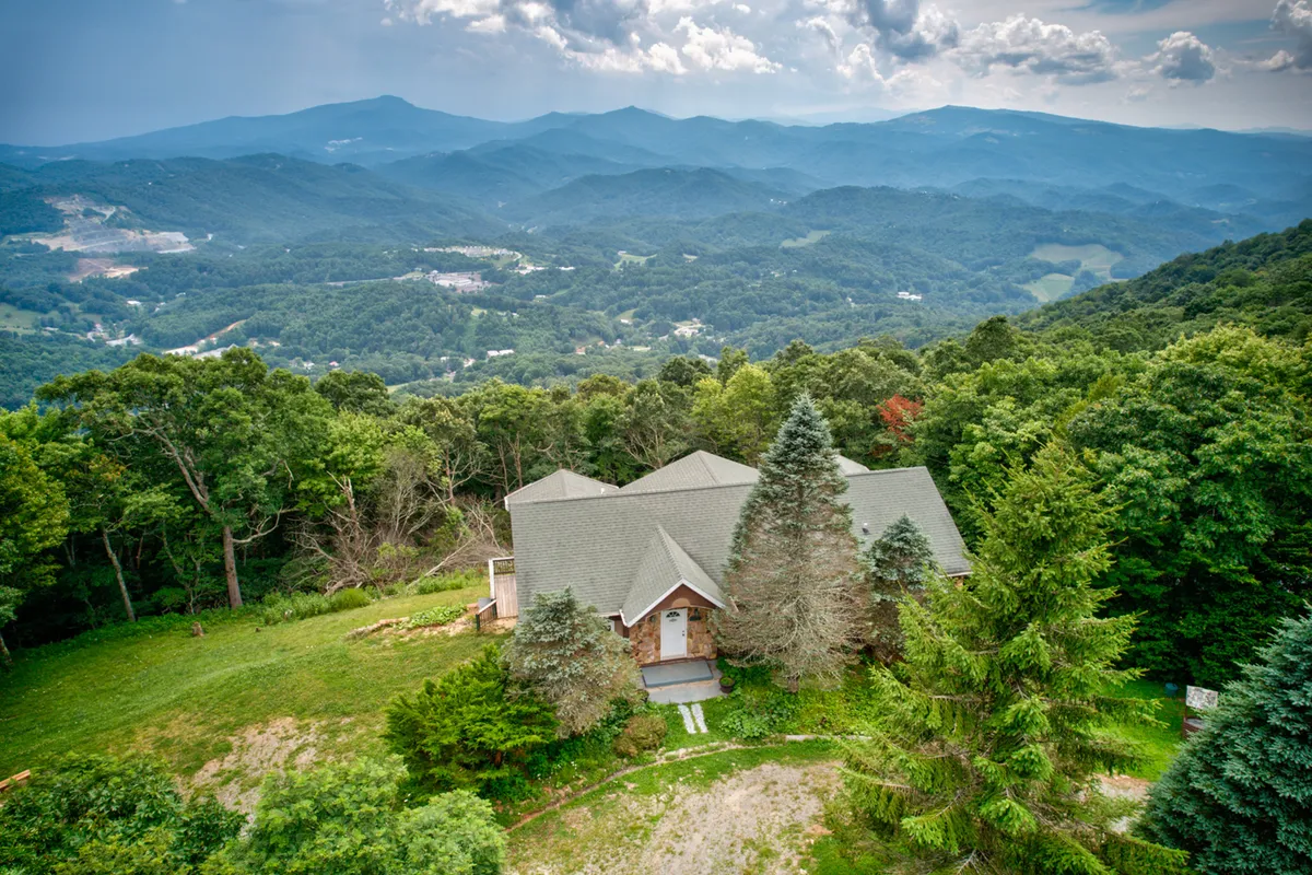 This image showcases the Shooting Star Lodge poised against a dramatic mountain range backdrop, surrounded by lush greenery and a winding driveway. The view emphasizes the lodge’s elevated position, offering sweeping vistas and context for outdoor activities like hiking and nature walks.
