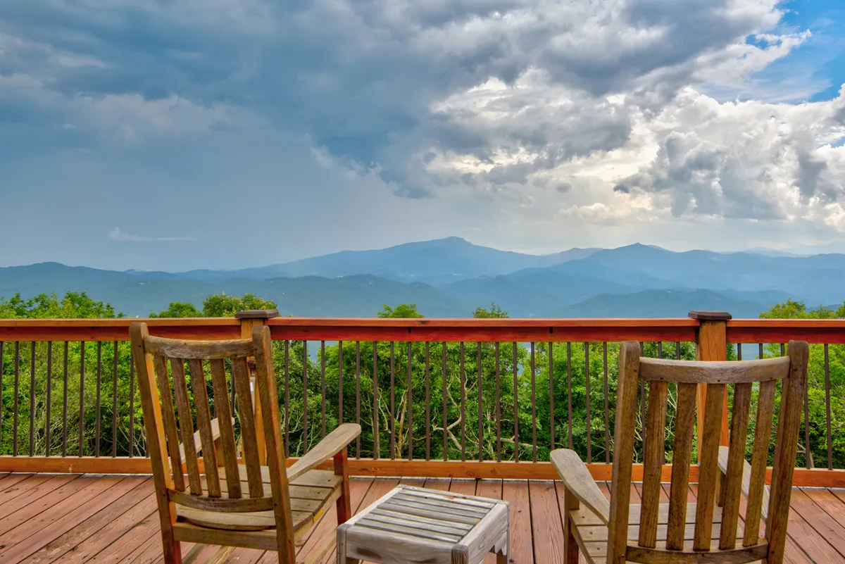Two classic wooden rocking chairs face outward from a deck, overlooking an expansive mountain landscape. The setting is tranquil and beckons for quiet moments of relaxation or sunset watching, ideal for guests and their pets to unwind together.