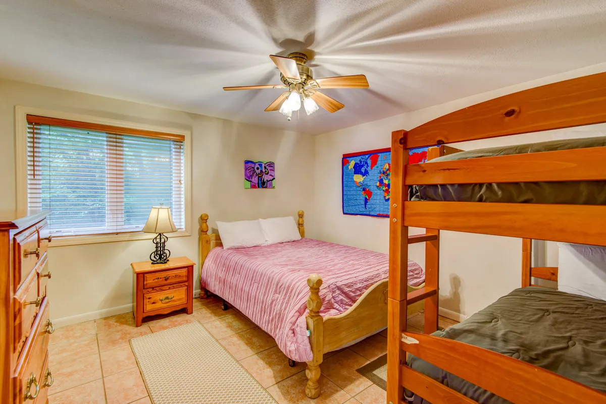 A cozy bedroom designed for families or groups, featuring a bunk bed and a full-size bed, colorful artwork, soft lighting, and a dresser. The mood is playful and welcoming, making it ideal for children or multiple guests.