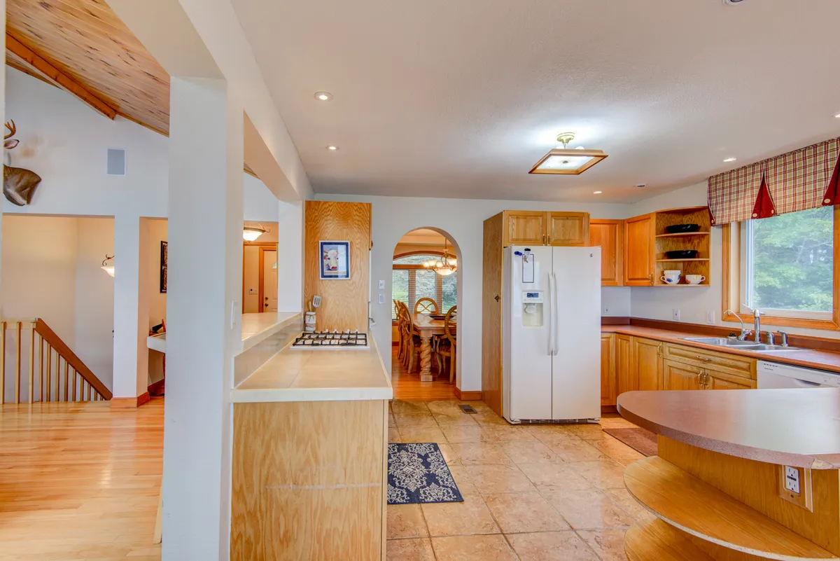 A cozy shared kitchen and dining area with a kitchen island, a spacious wooden table, and a large window letting in abundant natural light. The layout encourages communal meals, conversation, and family gatherings around the table.