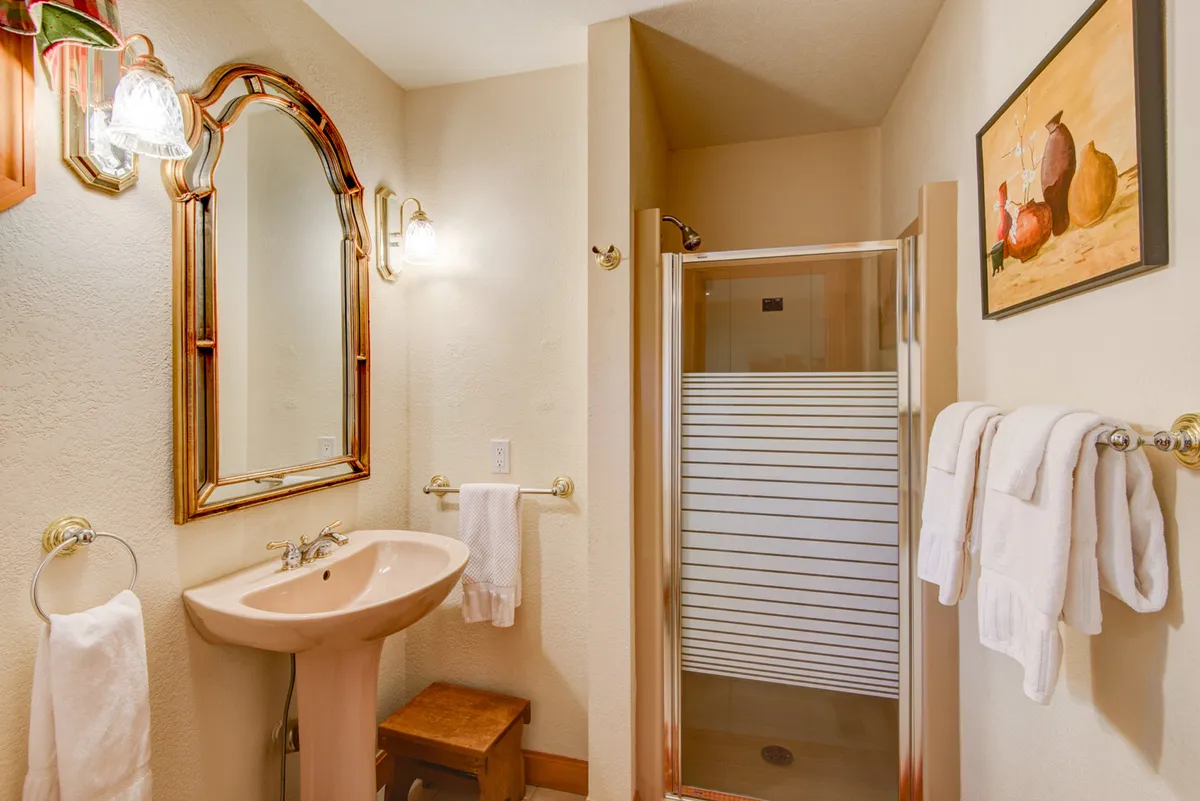 A serene bathroom with an elegant mirror, pedestal sink, glass shower enclosure, and tasteful decorative painting. The space is calm and inviting, echoing the promise of privacy and modern comfort throughout the property.