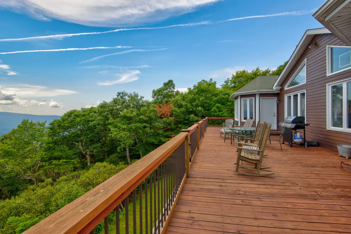 A serene wooden deck set against lush greenery and distant mountains, furnished with outdoor seating perfect for dining or relaxing. The setting invites guests to enjoy meals outdoors with breathtaking views and fresh mountain air.