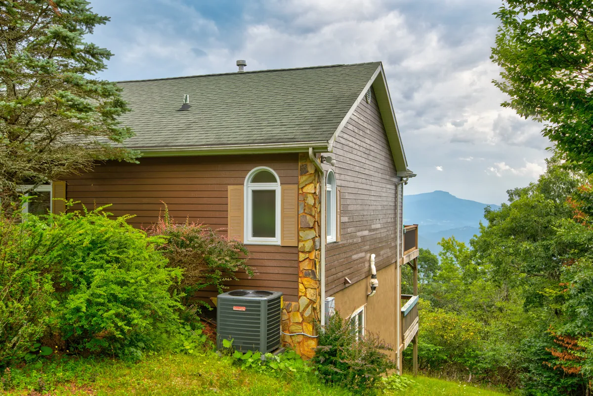 The lodge’s wooden exterior with stone accents is framed by landscaped greenery and a scenic mountain backdrop, suggesting a tranquil mountain retreat that’s still connected to nature. The image conveys a sense of arrival and the property’s inviting presence.