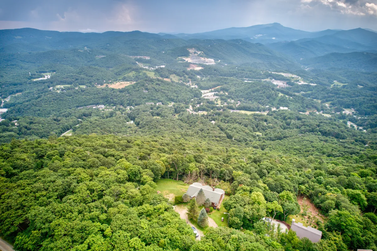 An expansive view of a forested valley and mountain range, with an isolated house nestled among the trees. The seasonal changes are visible, from lush foliage to snow-tipped peaks, evoking the area’s natural beauty and adventure potential.