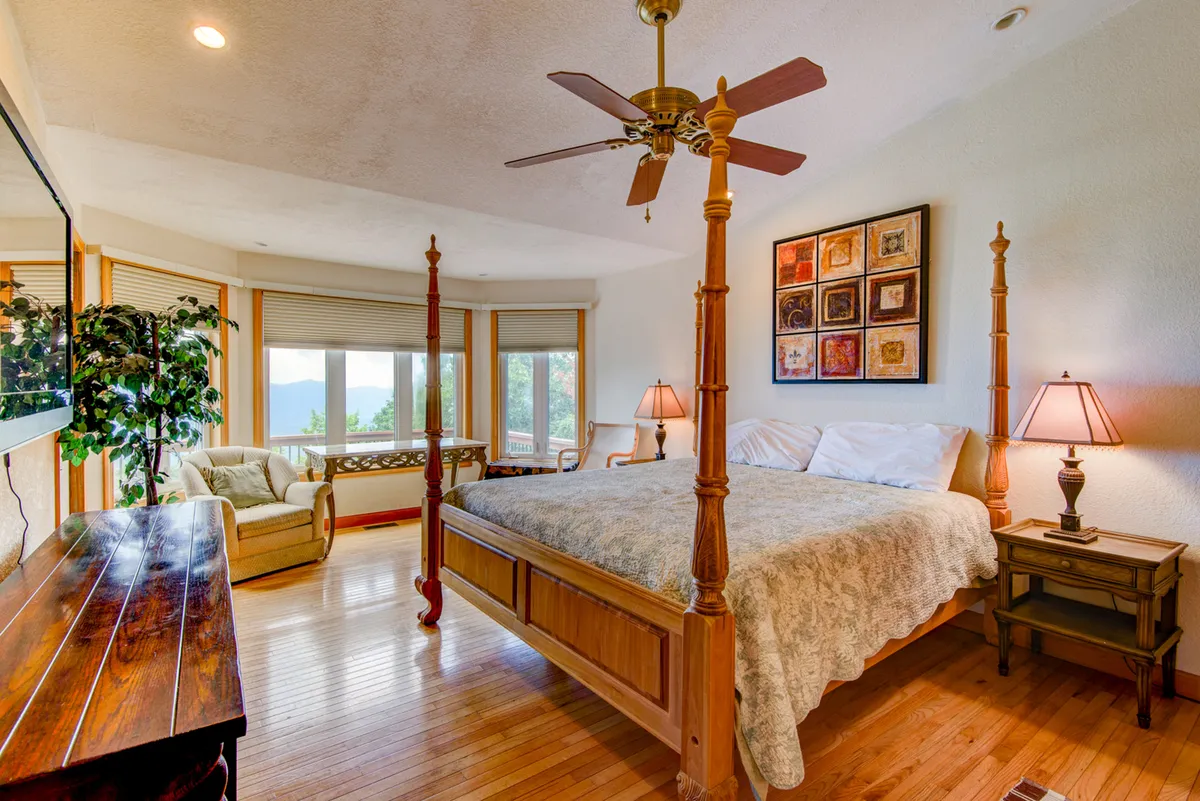 A tranquil bedroom featuring a classic four-poster bed positioned near a window with built-in seating, artfully decorated with soft lighting from lamps on nightstands and artwork on the wall. The room exudes a peaceful ambiance, perfect for unwinding after a day outdoors.